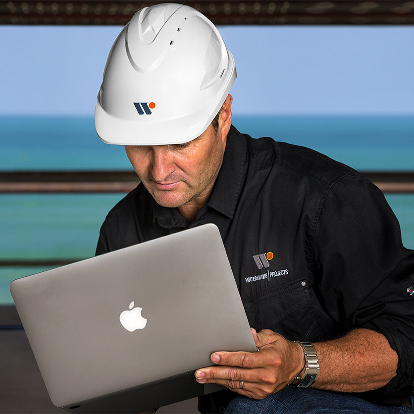 Engineer wearing a white safety helmet using a laptop at an industrial worksite in Adelaide, South Australia.