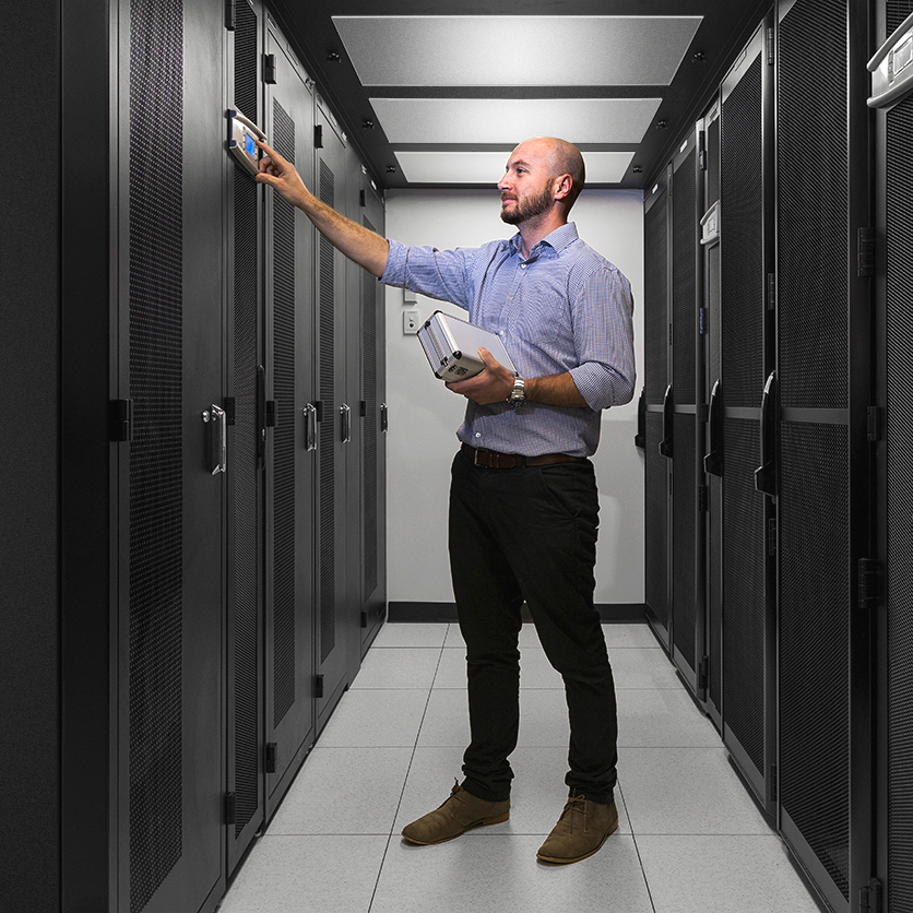 Engineer inspecting server cabinets inside a modern data centre using monitoring equipment in Adelaide, South Australia.