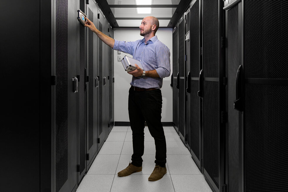 Commercial technology photograph of an engineer monitoring enterprise server infrastructure inside a secure data centre for business marketing and corporate communications.
