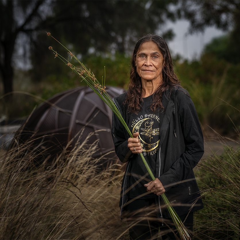 Environmental portrait of a woman holding native reeds in a natural bushland setting during a community cultural project in South Australia.