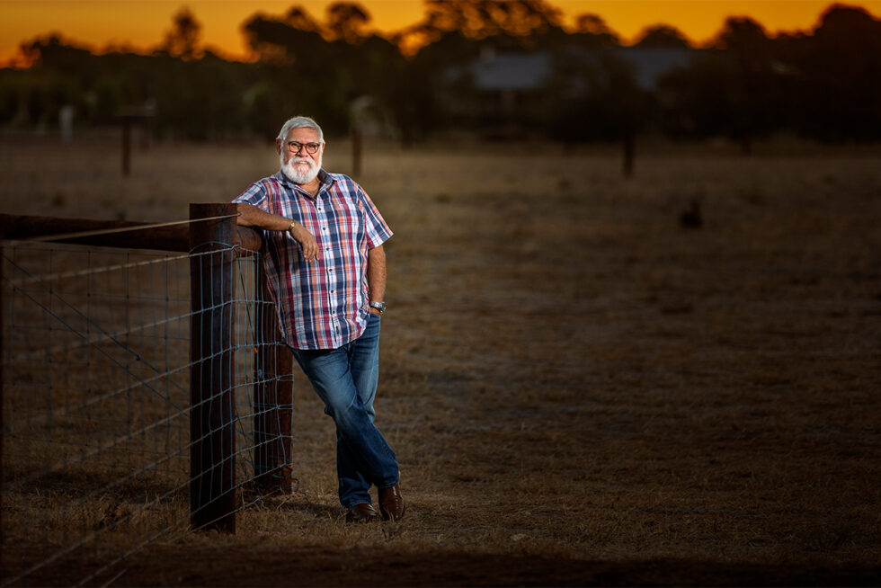 Portrait of a man leaning on a farm gate in a rural South Australian landscape at sunset.