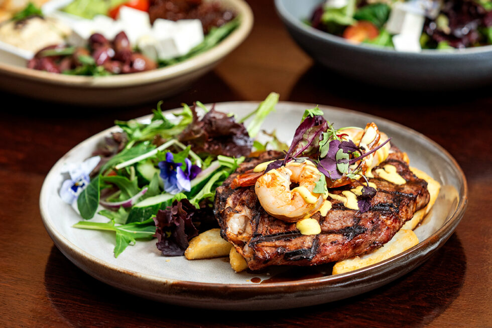 Professional food photograph of a grilled steak with prawns, chips, fresh salad, and gourmet presentation for restaurant marketing in Adelaide.