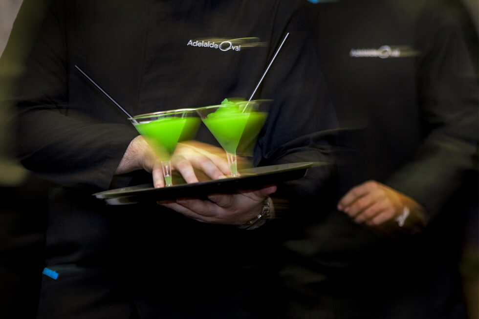 Creative commercial hospitality photograph of bright green cocktails being served with motion blur, highlighting premium customer service and bar atmosphere in Adelaide.