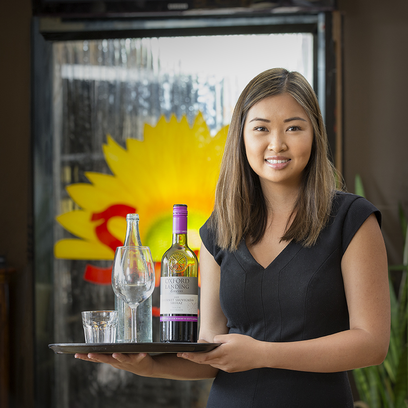 Hospitality staff member holding a tray with wine and glassware inside a restaurant in Adelaide, South Australia.