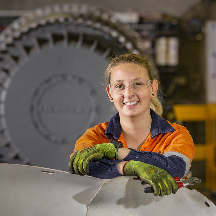 Portrait of a skilled tradesperson wearing safety glasses and high-visibility workwear inside a manufacturing workshop in Adelaide, South Australia.