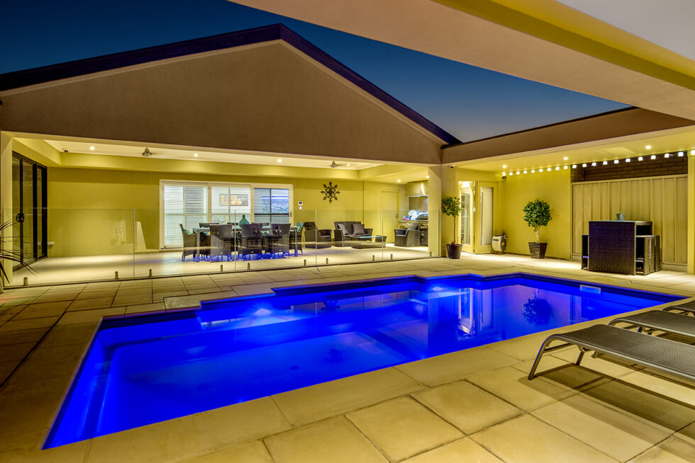 Contemporary luxury home with illuminated swimming pool, outdoor entertaining area, architectural lighting, and modern residential design photographed at twilight in Adelaide.