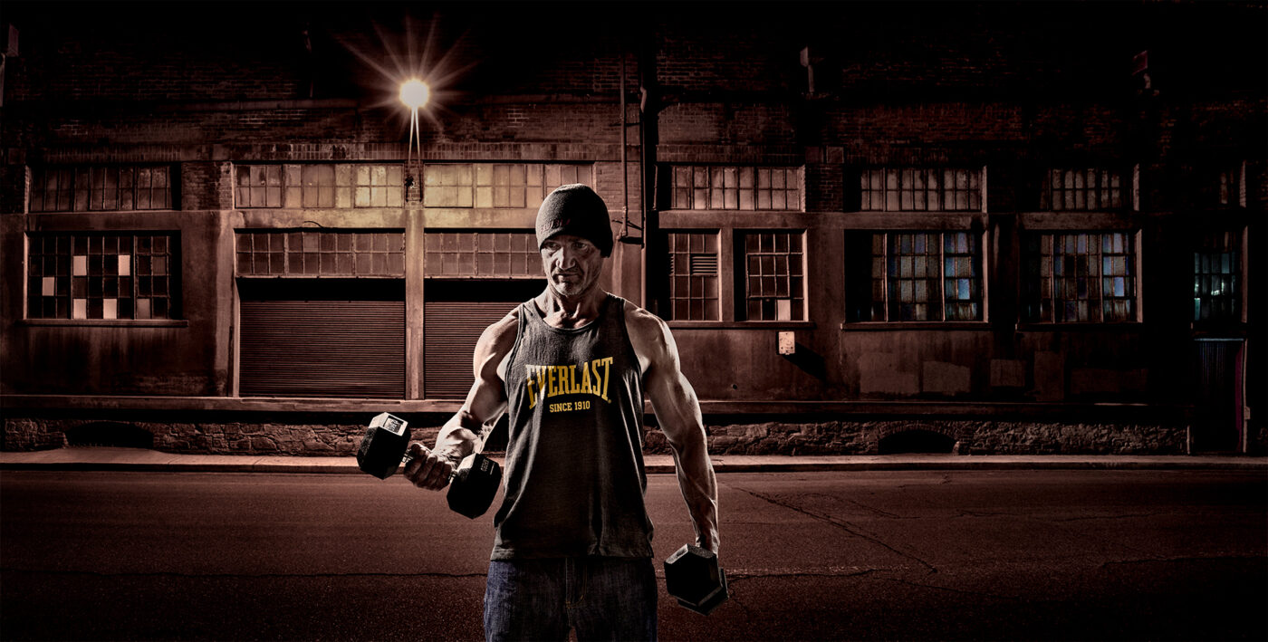 Dramatic urban fitness portrait of a man training with dumbbells in an industrial streetscape at night in Adelaide, South Australia.