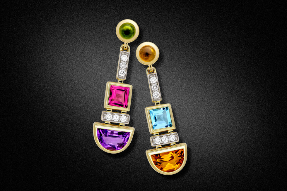 Professional jewellery product photograph of handcrafted gold earrings featuring coloured gemstones and diamond accents on a black background.